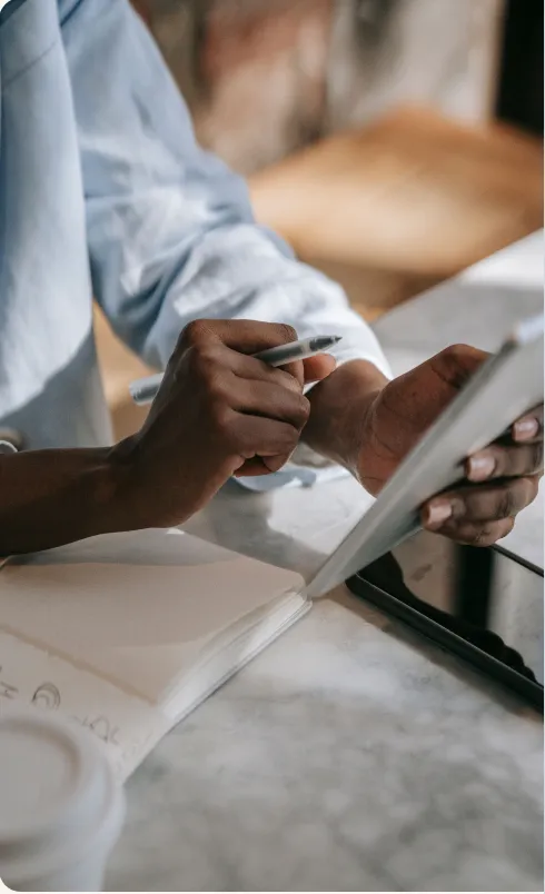 Person writing notes while reviewing data on a tablet